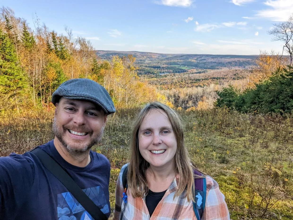 Gemma and JR stand in front of the views at Keppoch Mountain - a background of rolling hills highlighted with autumnal colours
