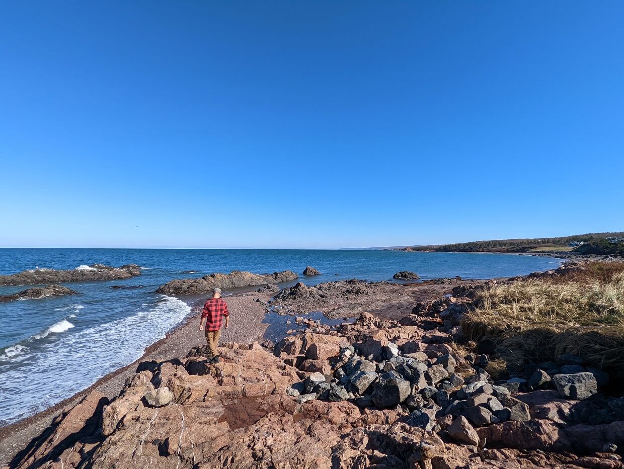 Back view of JR walking on rock near Arisaig Lighthouse with ocean and more rocks in background