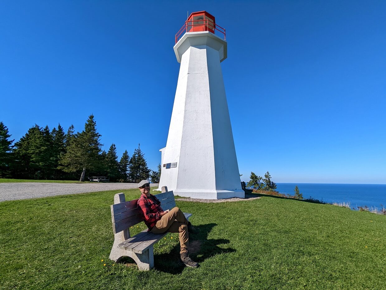 JR sat on beach in front of red and white Cape George Lighthouse on Cape George Scenic Drive