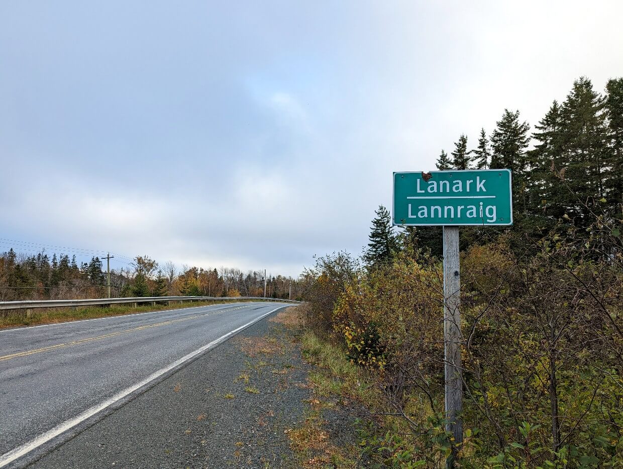 View of green Lanark road sign next to Cape George Scenic Drive, with Gaelic translation 'Lannraig'
