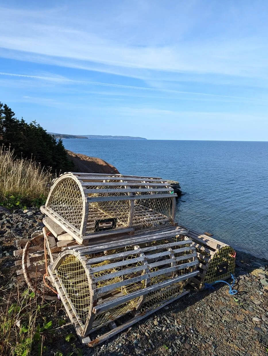 Close up of lobster traps on cliffside with ocean behind, views of Cape George Scenic Drive ahead