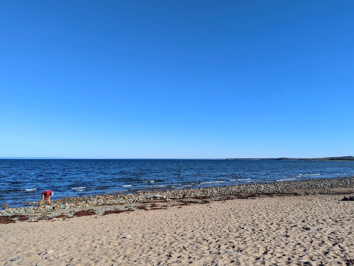 Looking across sandy Mahoneys Beach to JR picking up something, while standing in front of relatively calm ocean