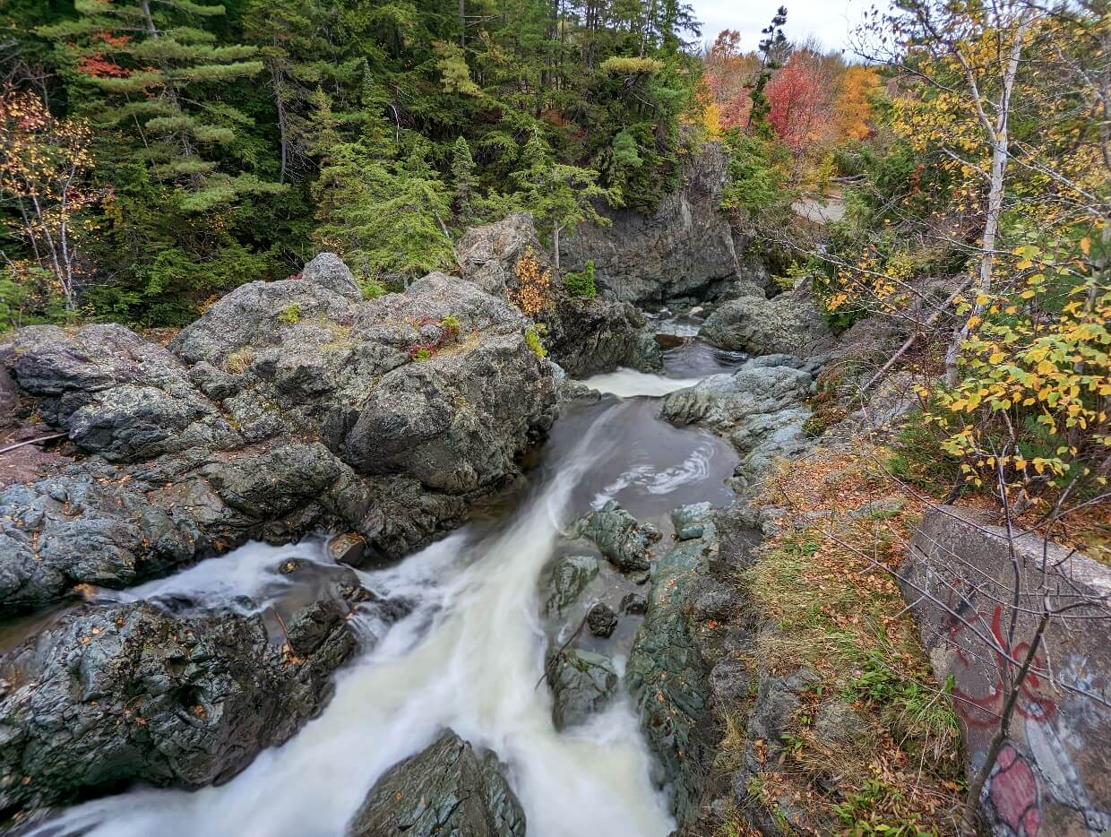 Looking down on Park Falls from bridge, where a strong cascade flows over and through rock canyon, with some autumn colours in background