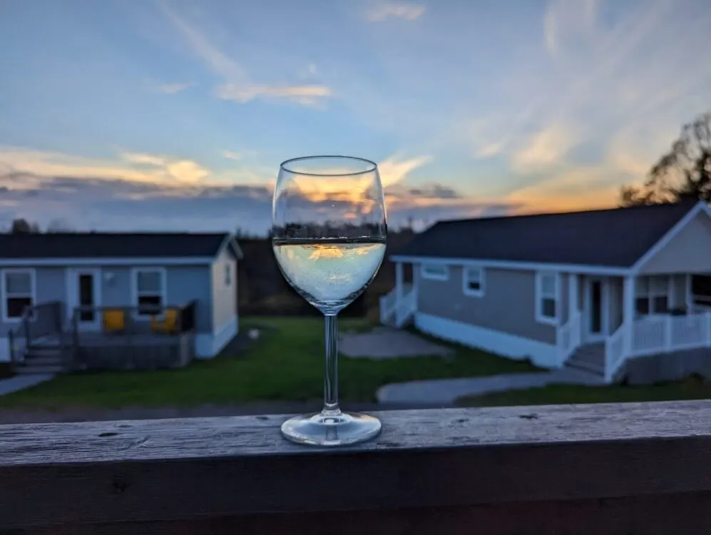 Close up of white wine glass in front of cottage buildings at Fossil Farms with sunset in background