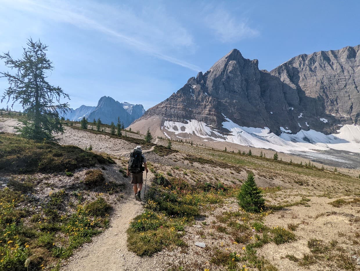 Back view of JR hiking on the Rockwall Trail, heading towards huge rock cliff