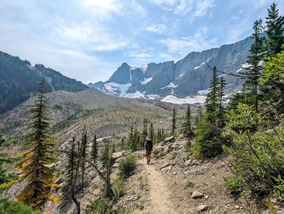 Back view of JR descending dirt path towards Tumbling Creek, with Tumbling Glacier and Rockwall in background