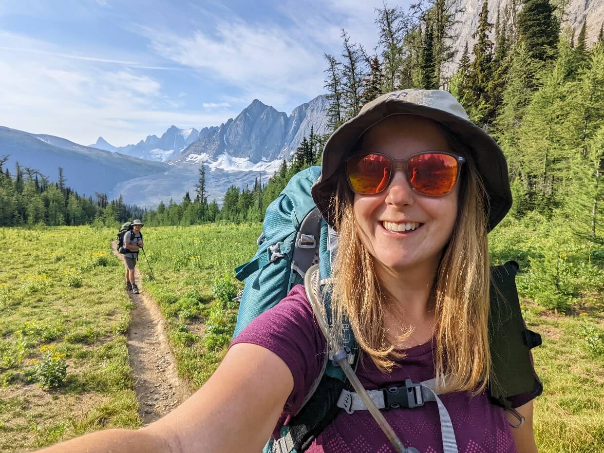 Selfie of Gemma and JR hiking the Rockwall Trail, with alpine meadows and huge rockface in background
