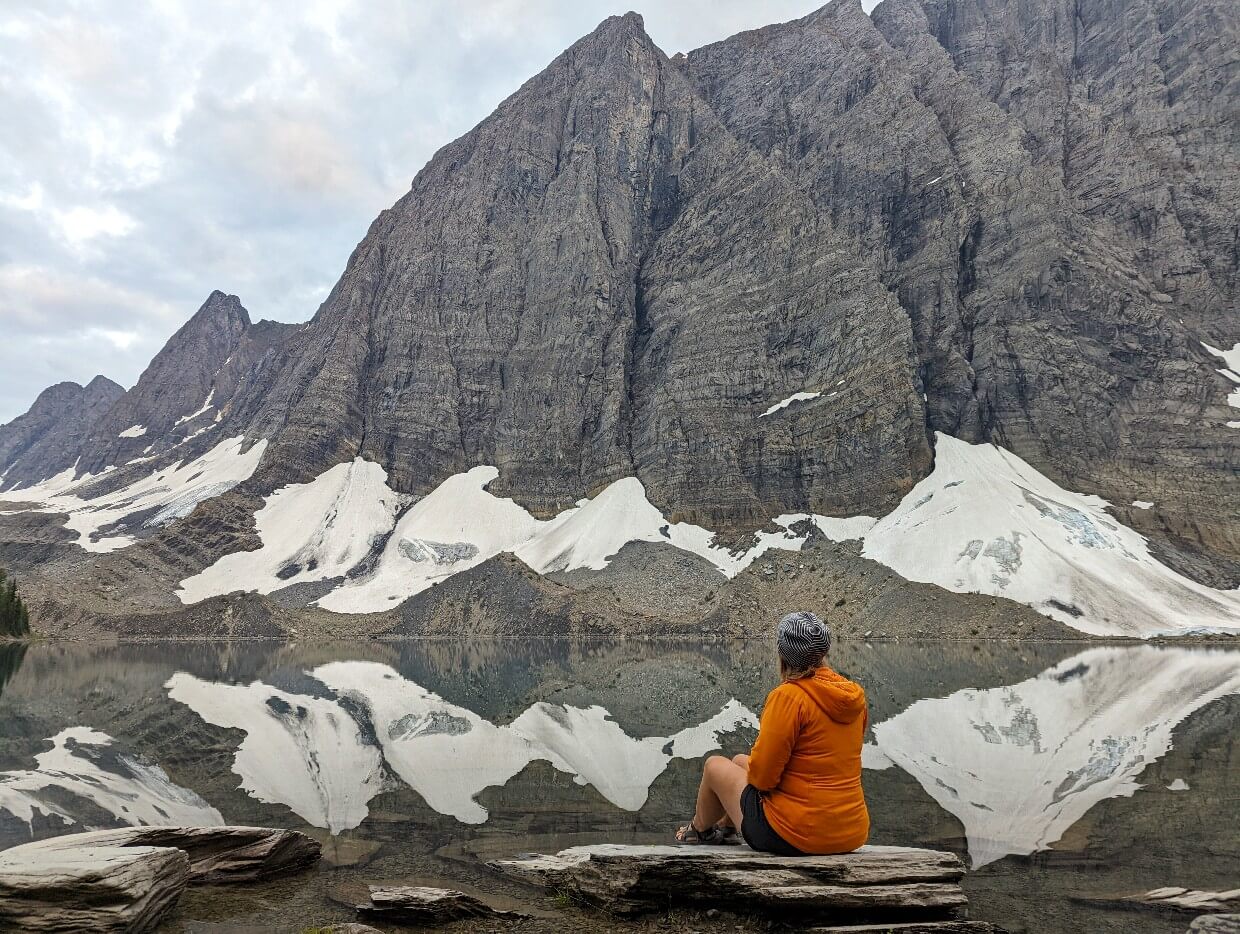 Back view of Gemma sat on a rock next to Floe Lake, with towering mountains above