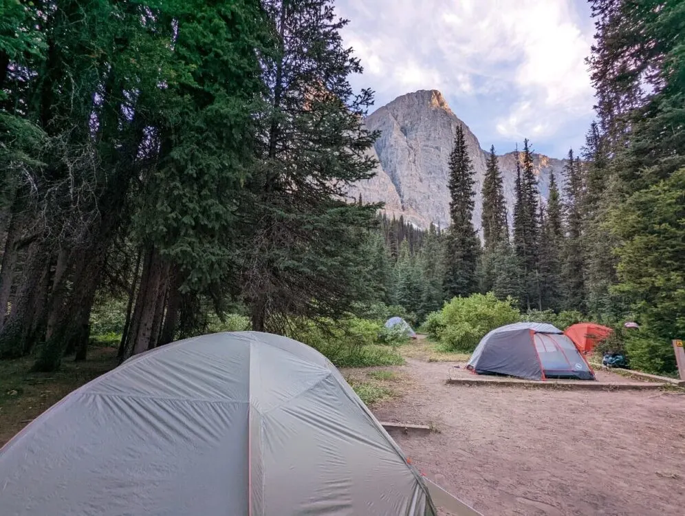 Looking across tent pads filled with tents in the Helmet Falls campground, with mountain peaks visible in the background