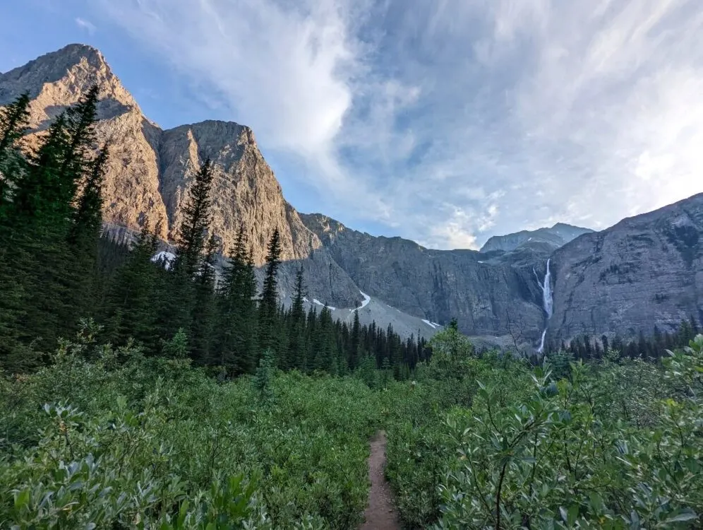 Looking up at an amphitheater of rock above forest, with large waterfall on right