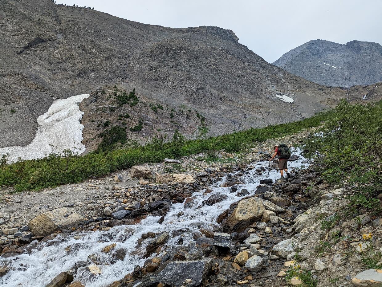 Back view of JR crossing a cascading river on the Rockwall Trail