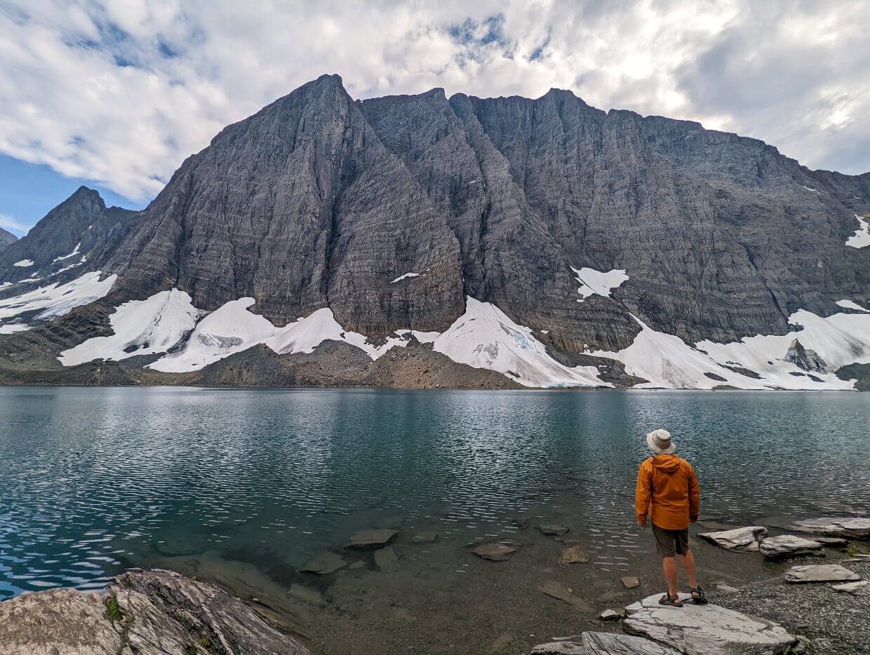 Back view of JR standing on the shore of Floe Lake, with calm lake surface and huge mountains towering above