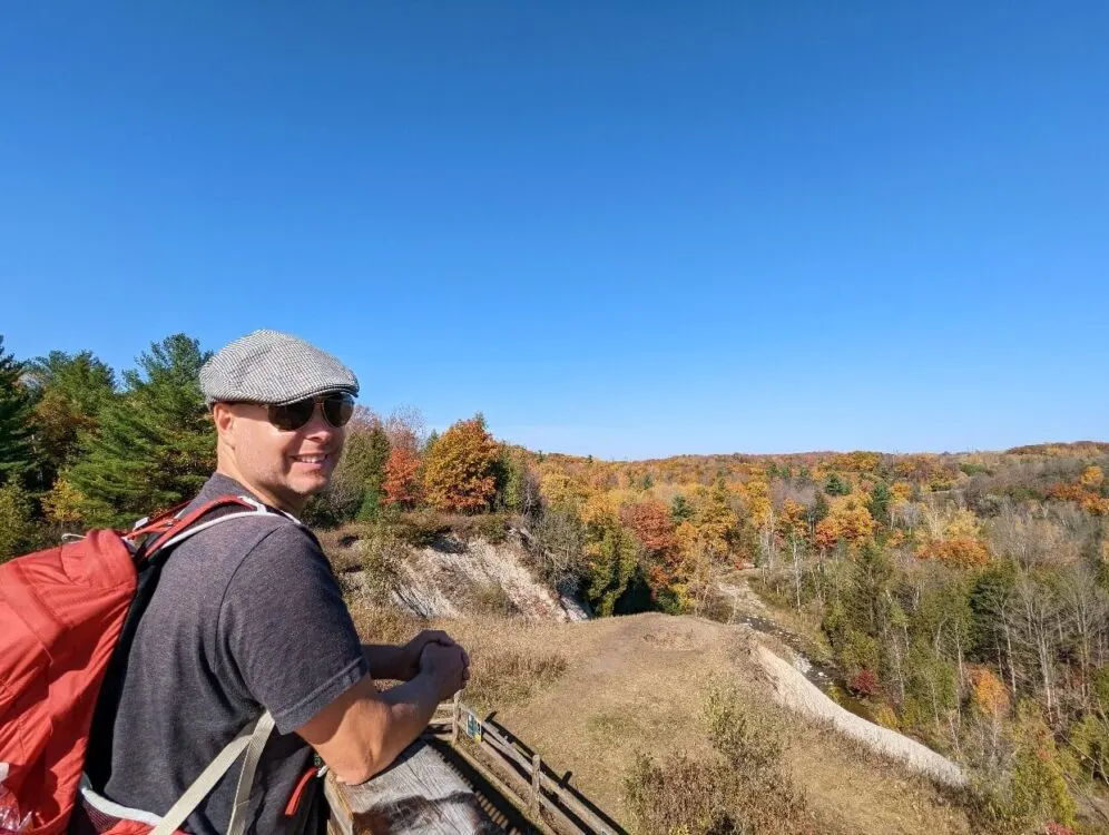 Side profile of JR looking at camera at lookout on Vista Trail (Rouge National Urban Park), with colourful autumnal trees in background