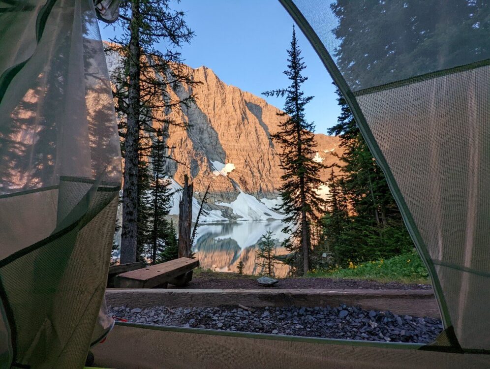 View through tent door of Floe lake, with morning sun on mountains behind lake
