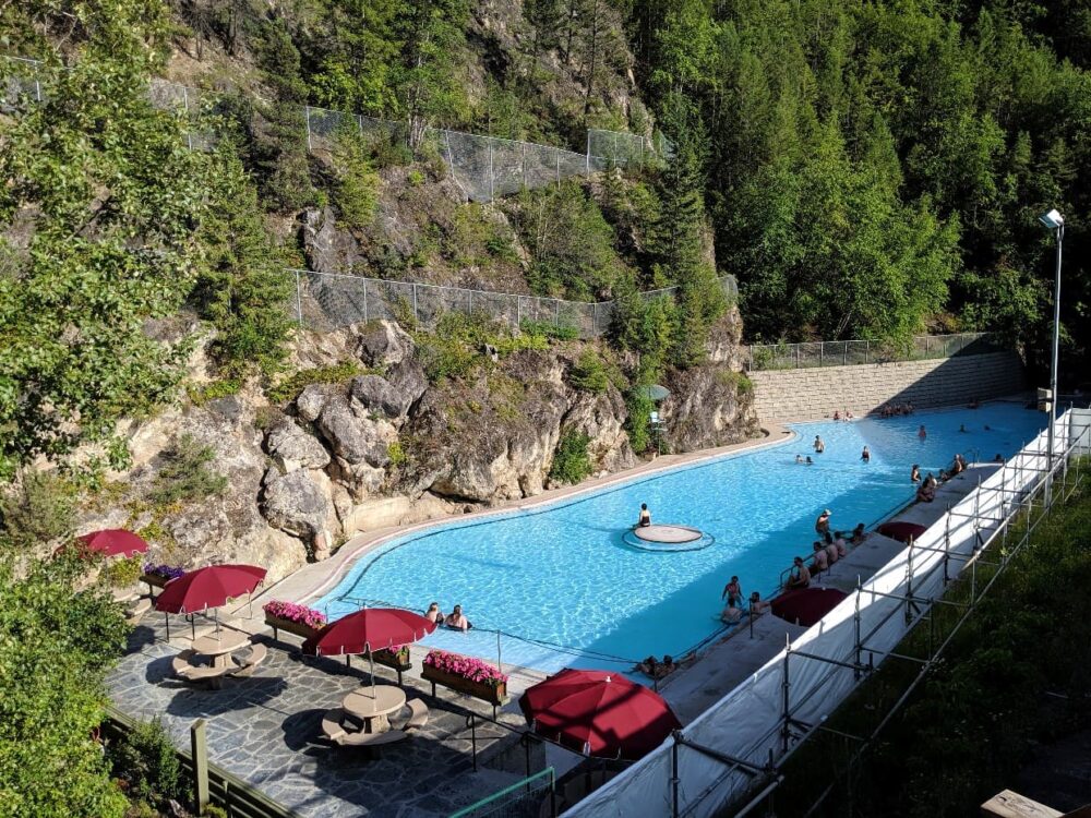 A long blue swimming pool sits in a canyon, with tables and umbrellas on the adjacent patio
