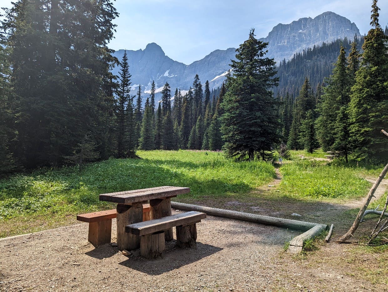 A small wooden bench and table sits in front of mountain views in the Tumbling Creek campground