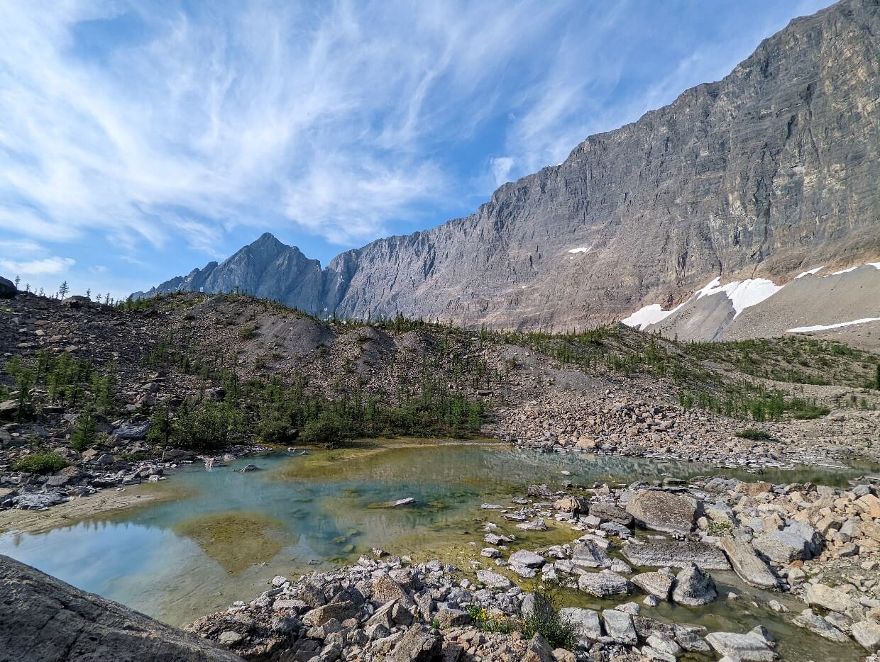 Looking across rocky tarn on the Rockwall Trail, with huge cliff behind