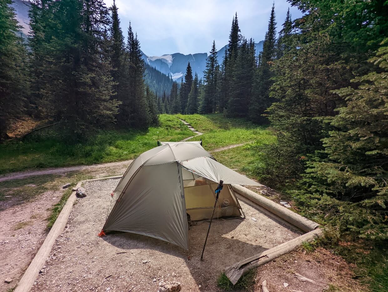 A set up tent on framed dirt tent pad in the Tumbling Creek campground, with view of glacier in background