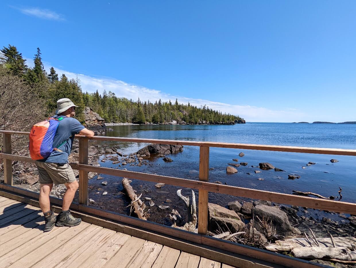 JR stands facing Lake Superior on bridge on a sunny June day while hiking the Top of the Giant Trail