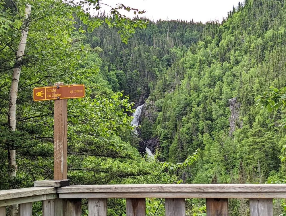 Wooden platform viewswith Chute du Diable sign, in front of cascading waterfall in forest