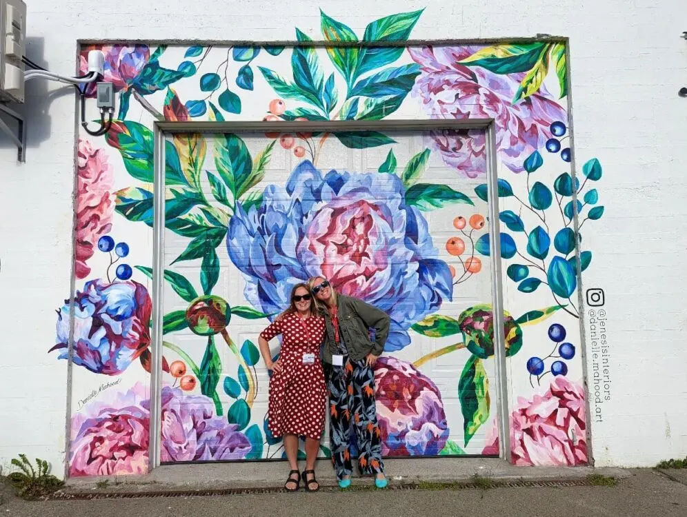 Gemma and Lindsay stand in front of a colouful flower mural on Yarmouth street