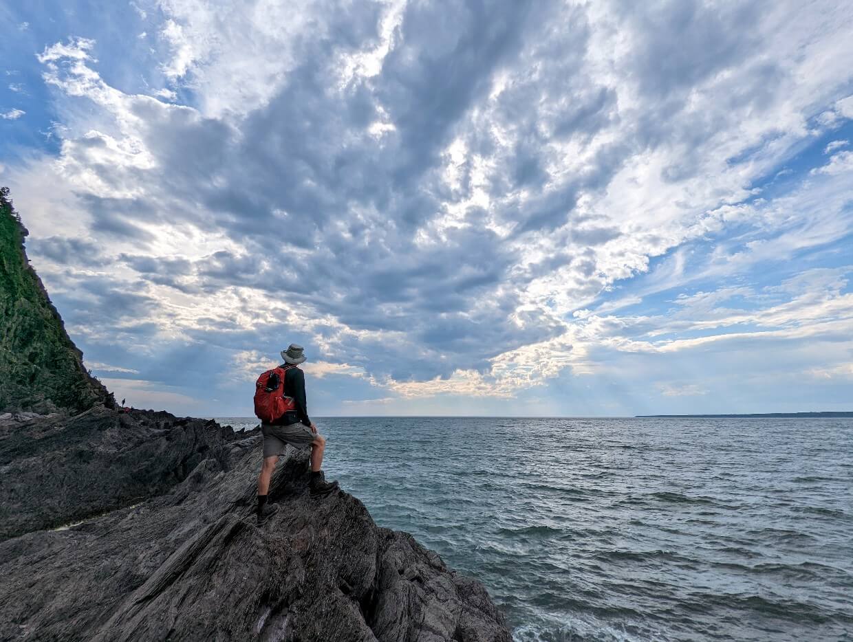 Back view of JR standing on jagged rocks next to coastline in Parc du Bic on the Cap-à-l'Orignal (a premier Gaspe Peninsula hiking trail)