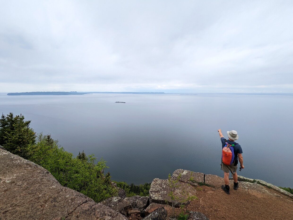 Back view of JR standing close to edge of cliff pointing out to Lake Superior, which sits 300m below