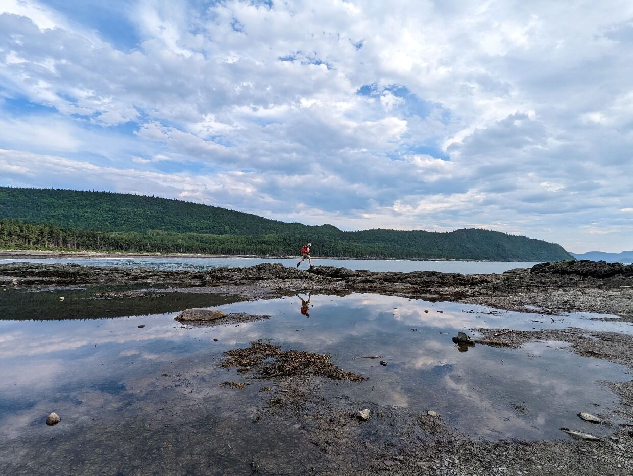 Looking across wide rockpool in Parc du Bic, with JR leaping over rocks in background. The rockpool surface is reflective