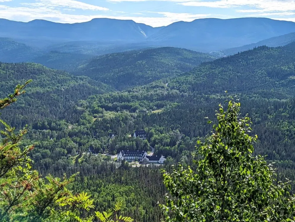 Elevated viewpoint looking down through trees to large hotel building in Parc national de la Gaspésie, surrounded by rolling forested hills