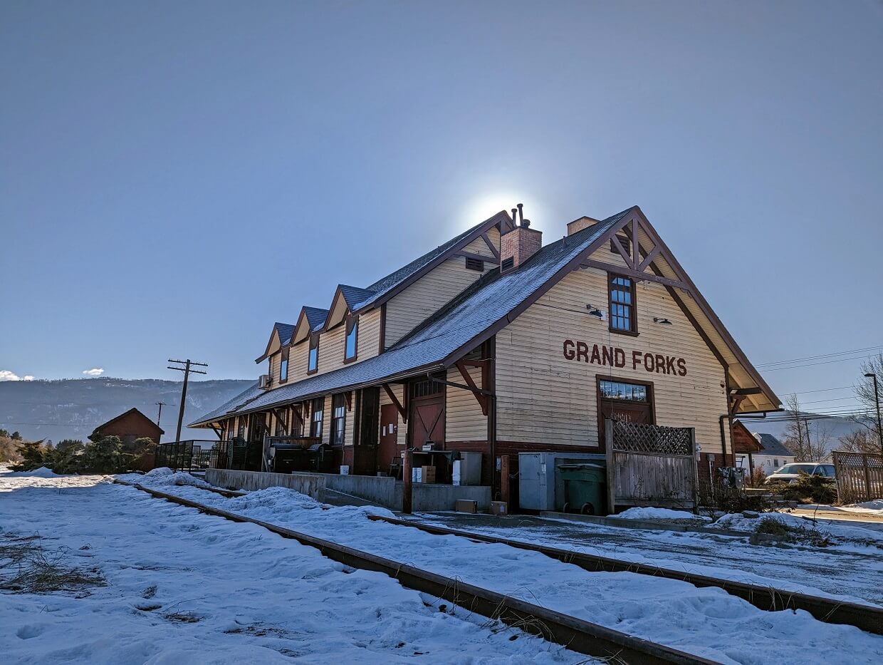 Looking up at Grand Forks Station Pub building on a sunny day, a two story building next to snowy railway tracks