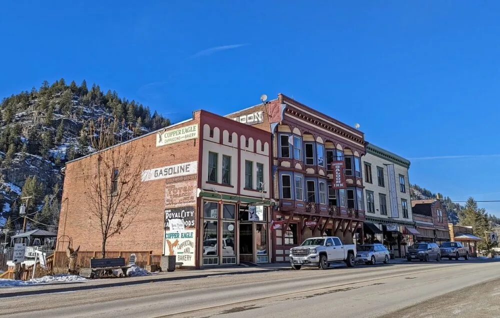 Heritage buildings in Greenwood next to Highway 3, with parked vehicles alongside road. There is a snowy mountain in the background