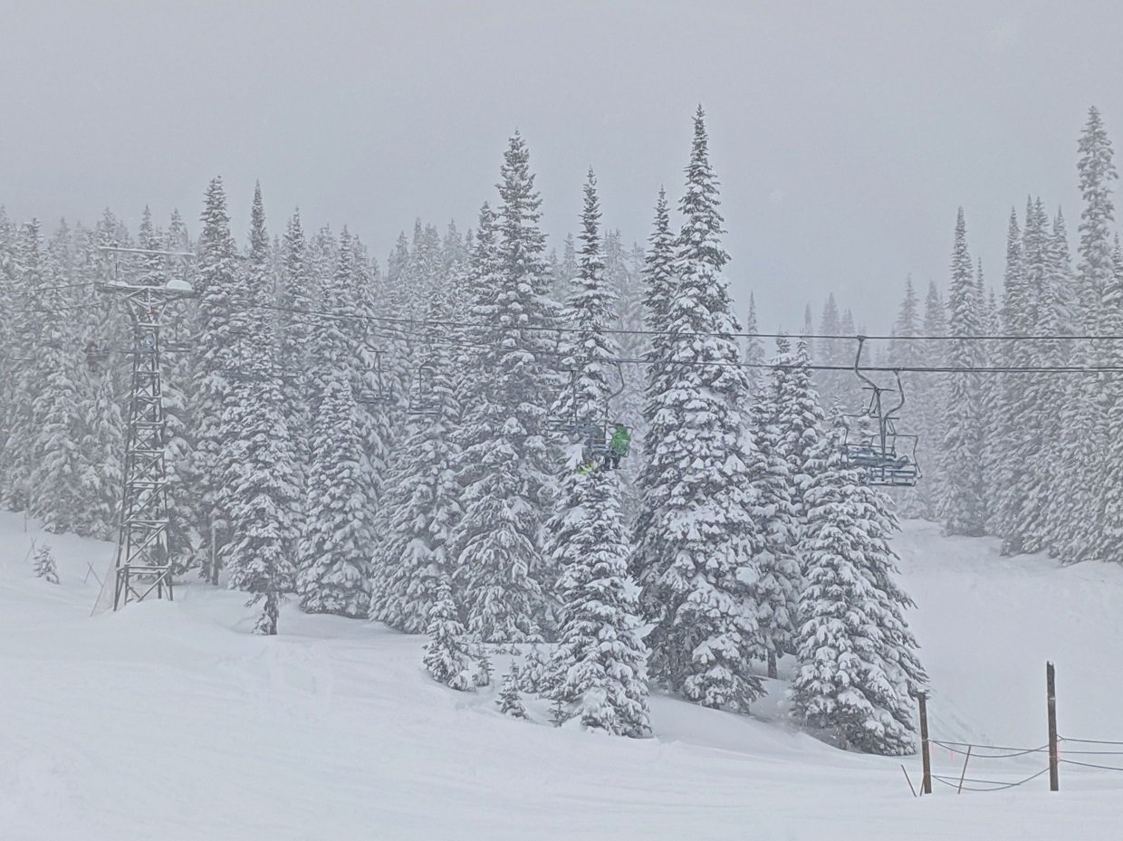 Two figures sit on chairlift at Baldy Mountain Resort, with very snowy trees in background