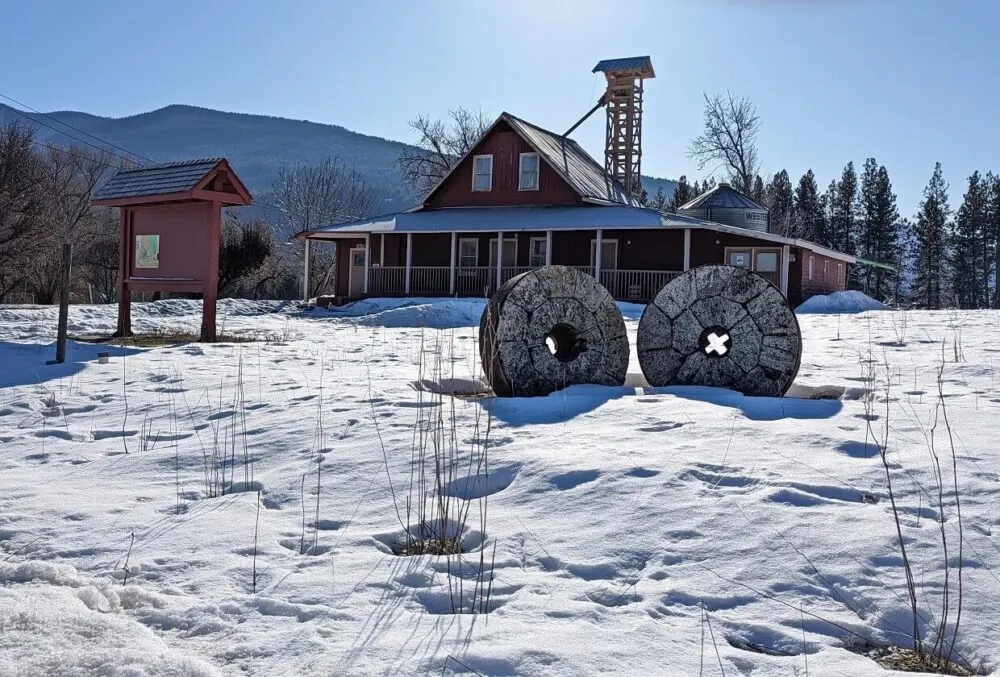 Looking across snowy field to mill stones in front of wooden flour mill building in Grand Forks