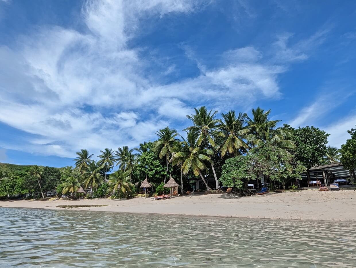 Water view of Blue Lagoon resort with clam ocean, loungers on beach and palm trees on shore