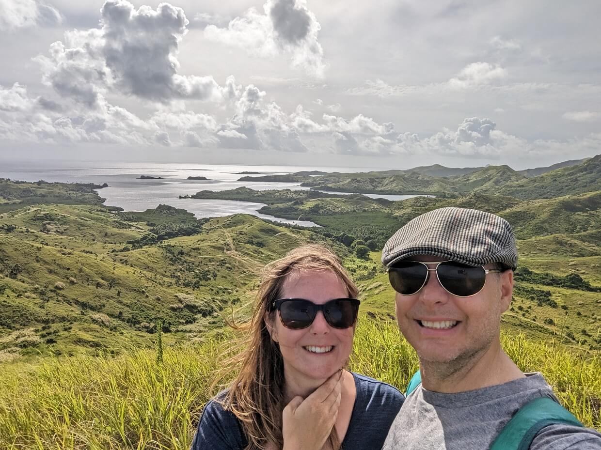 Selfie of Gemma and JR in front of volcanic island landscape in FIji, with cloudy skies