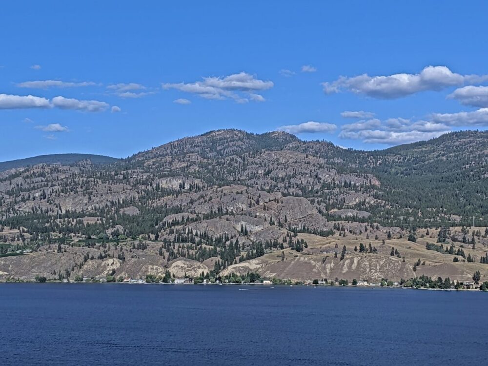 Elevated view looking across calm Skaha Lake to rugged canyons, mountains and forest area on other side