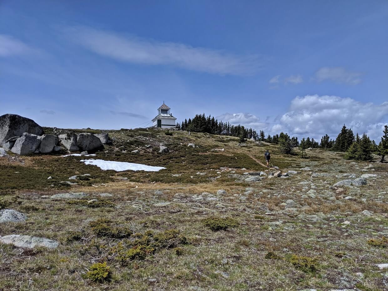 Back view of hiker on Brent Mountain Trail with white firetower in the background