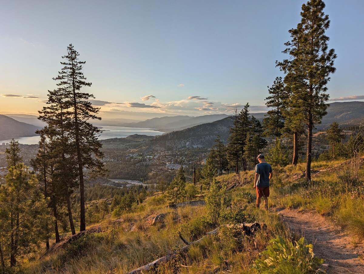 Back view of JR walking down G Spot Trail during golden area with views of Penticton and Okanagan lake below