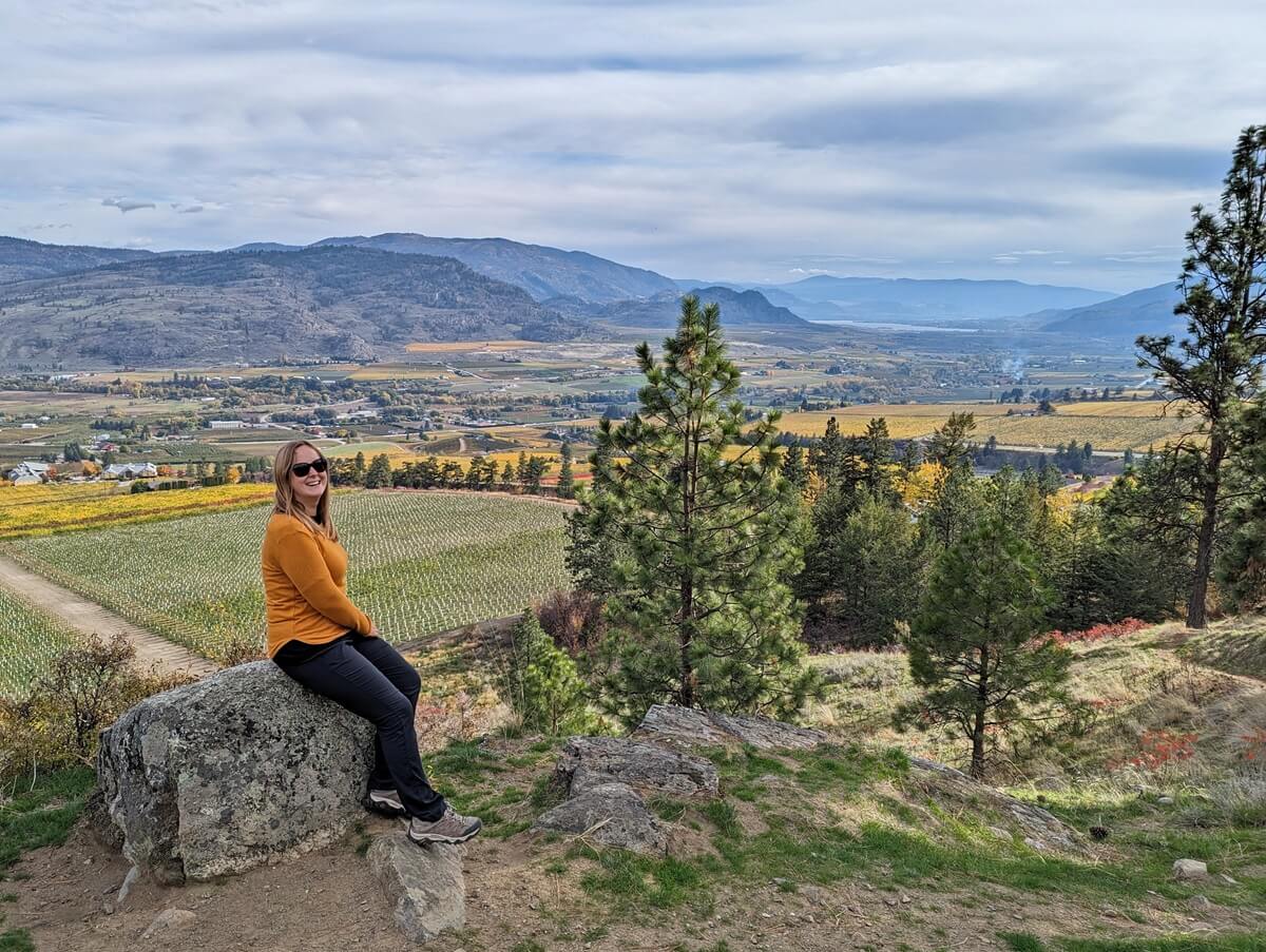 Back view of Gemma sitting ona rock at Golden Mile viewpoint in Oliver, with endless vineyards below