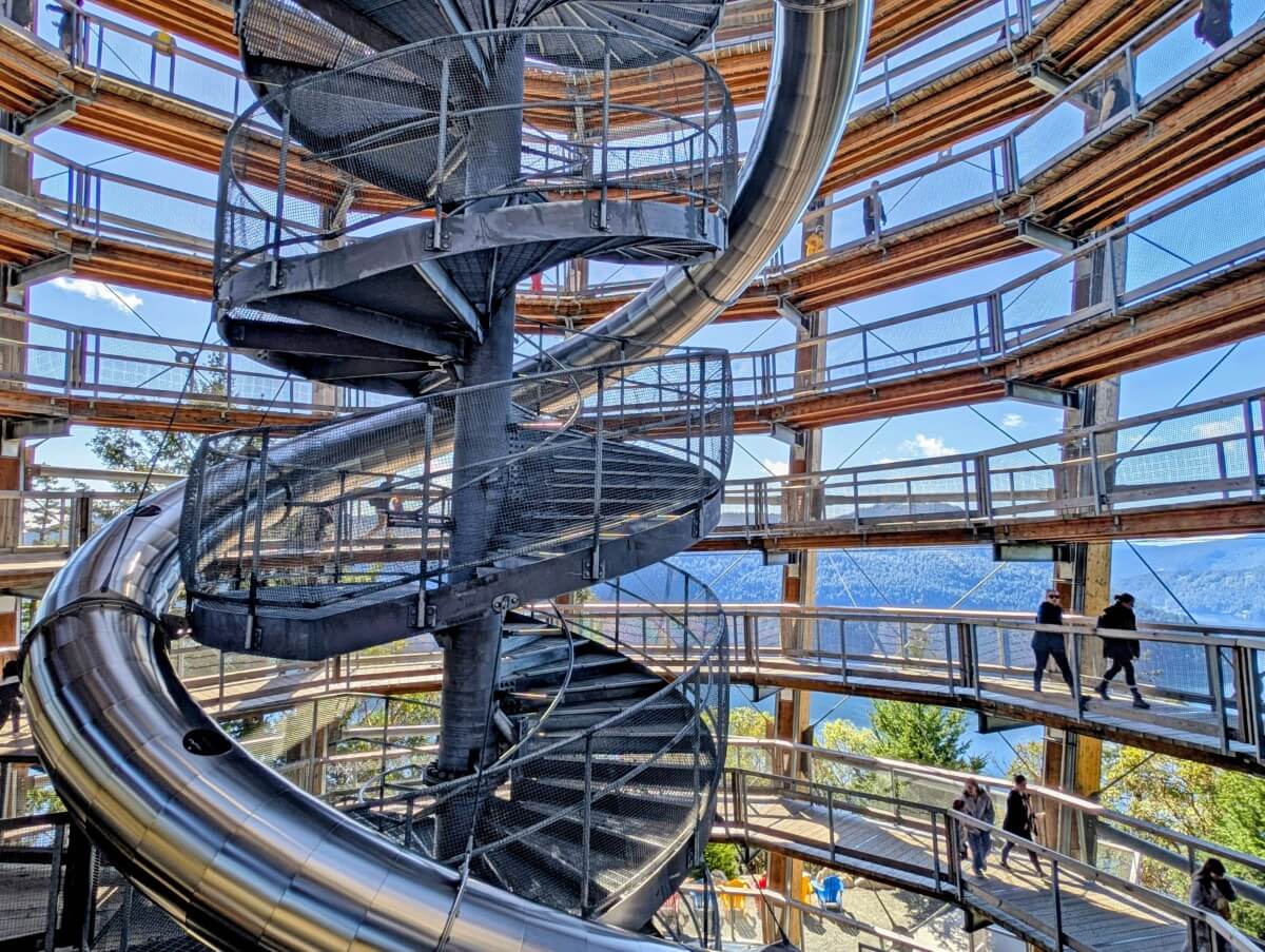 Inside the SkyWalk Spiral Tower with a metal circular staircase and slide through the middle of an airy wooden structure with views of a forested inlet behind