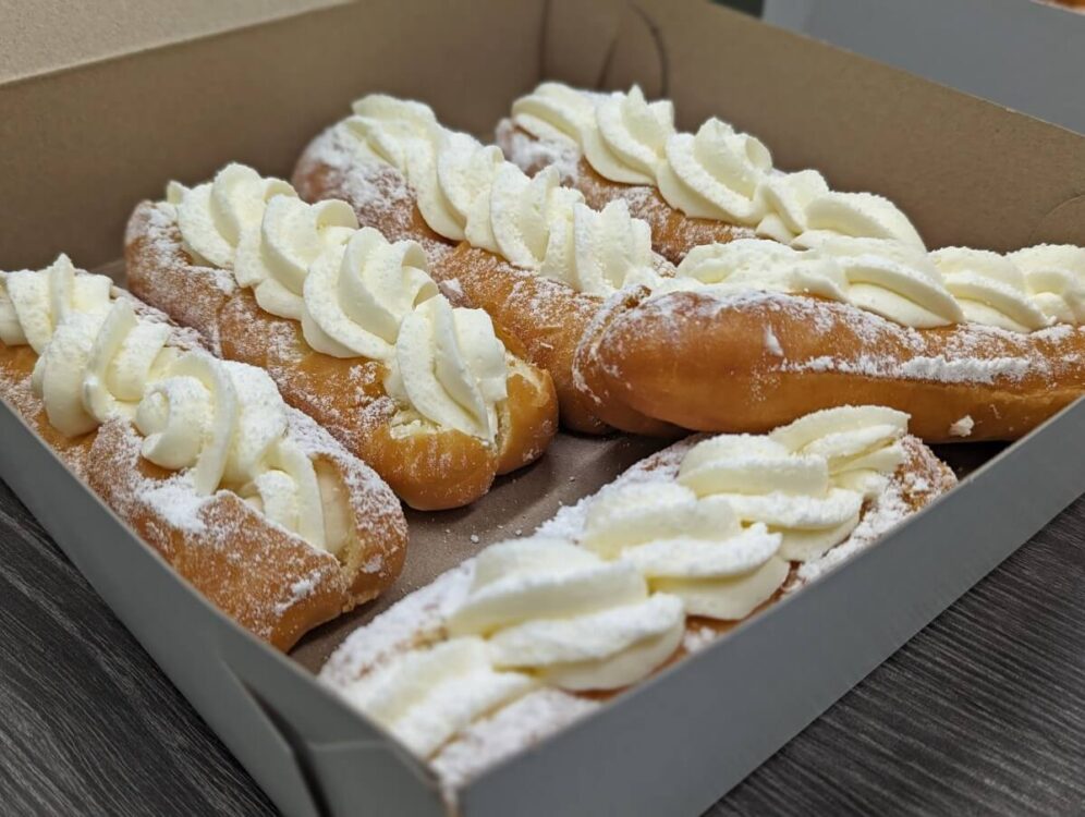 Close up of six cream filled Long John doughnuts in paper box