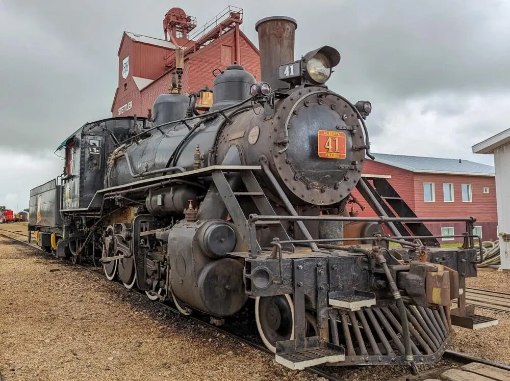 Close up of Alberta Prairie Railway steam locomative, with dark red grain elevator building in background