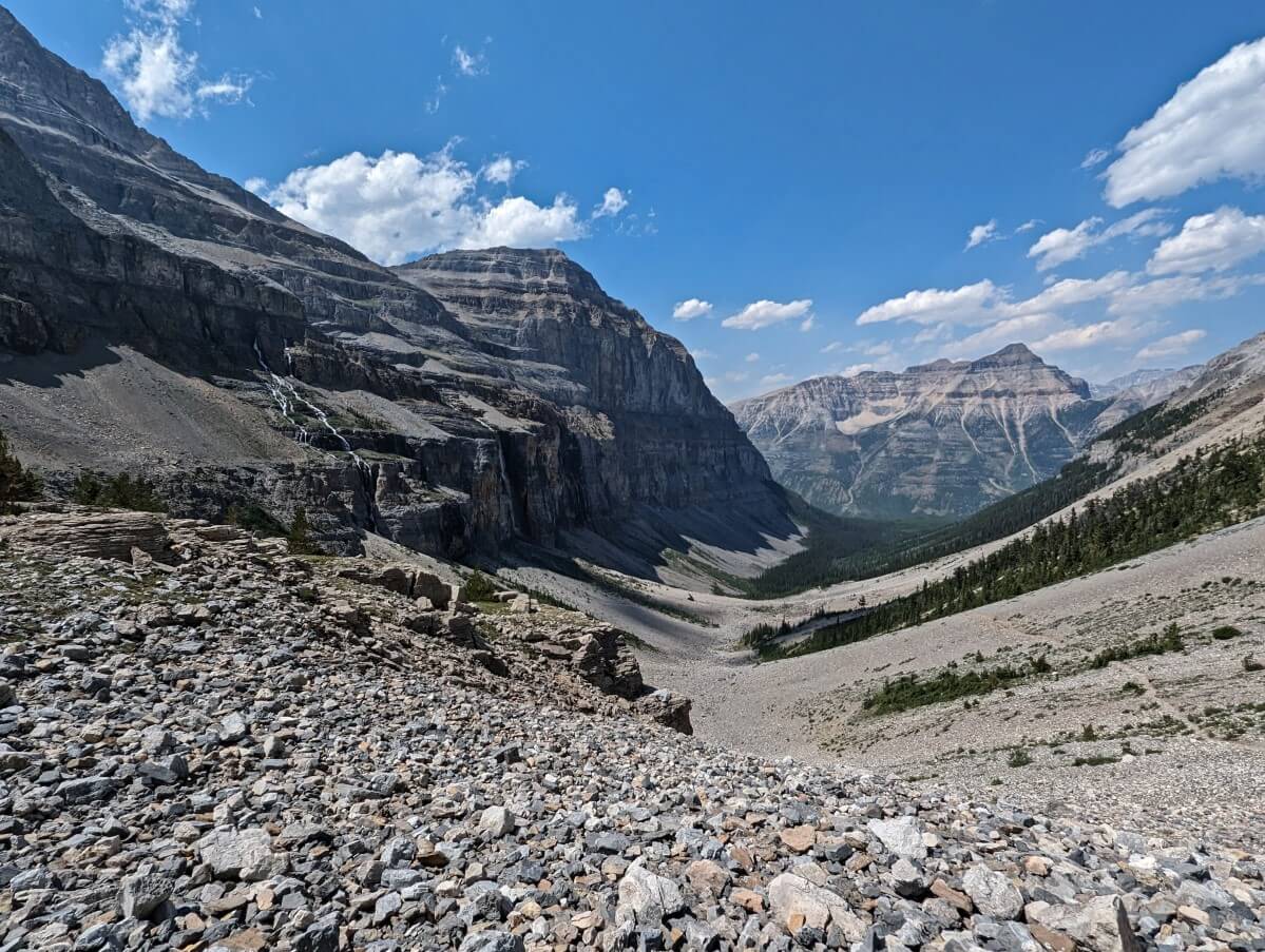 Looking down from Stanley Glacier upper basin to lower basin with multiple waterfalls and steep cliffs on left, mountain in background