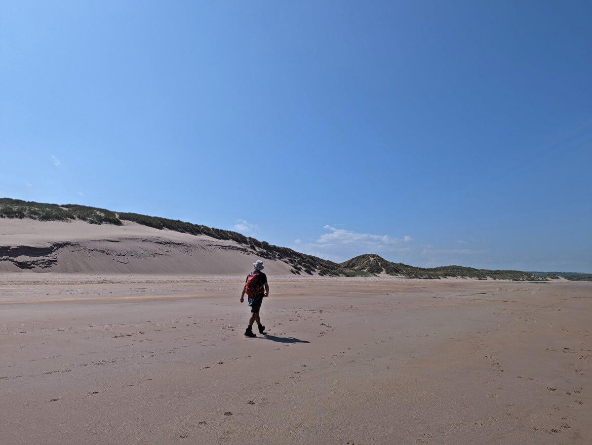 Back view of JR walking along sandy beach looking at sand dunes on Cheswick Sands
