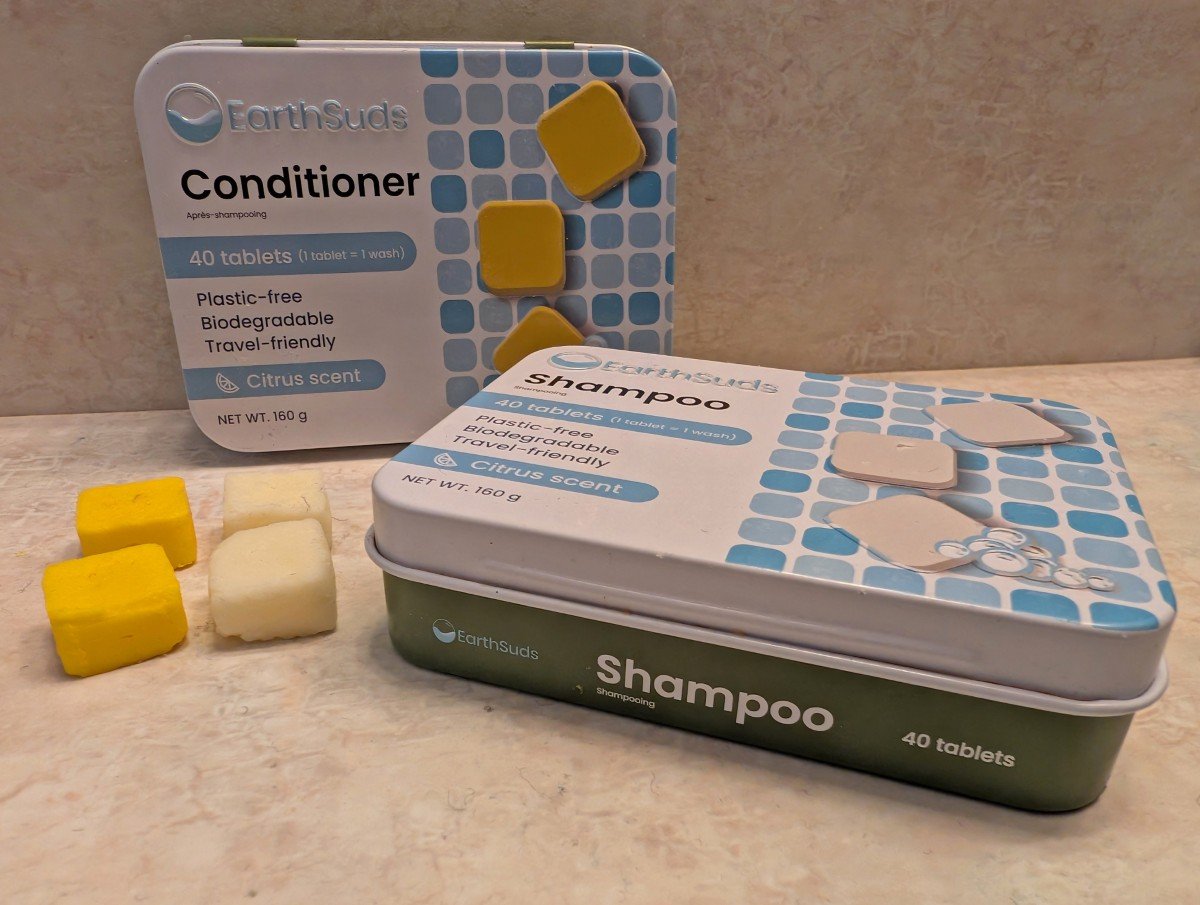 Two EarthSuds tins on bathroom surface with yellow conditioner cubes and white shampoo cubes