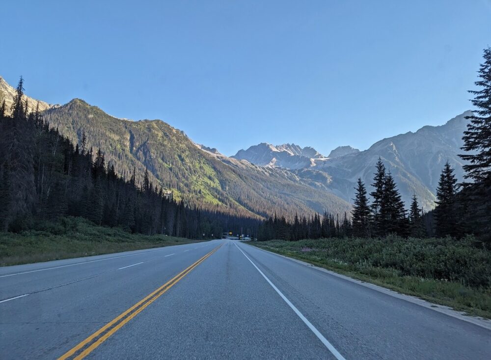 Vehicle view of Highway 1 through Glacier National Park, backdropped by mountains with forested slopes