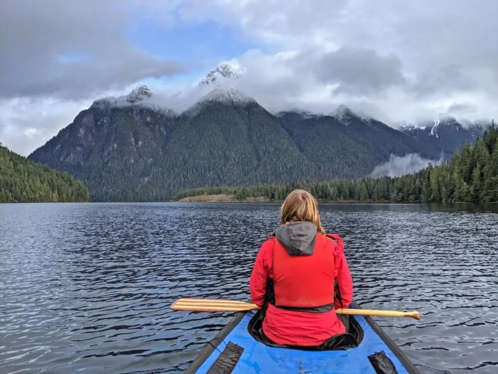 Back view of Gemma in canoe on calm Schoen Lake, which features tall snow capped mountains ahead