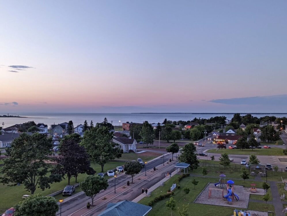 View from the ferris wheel at sunset at Shippagan cirque, with playground, housing, street parking and ocean in the backcountry