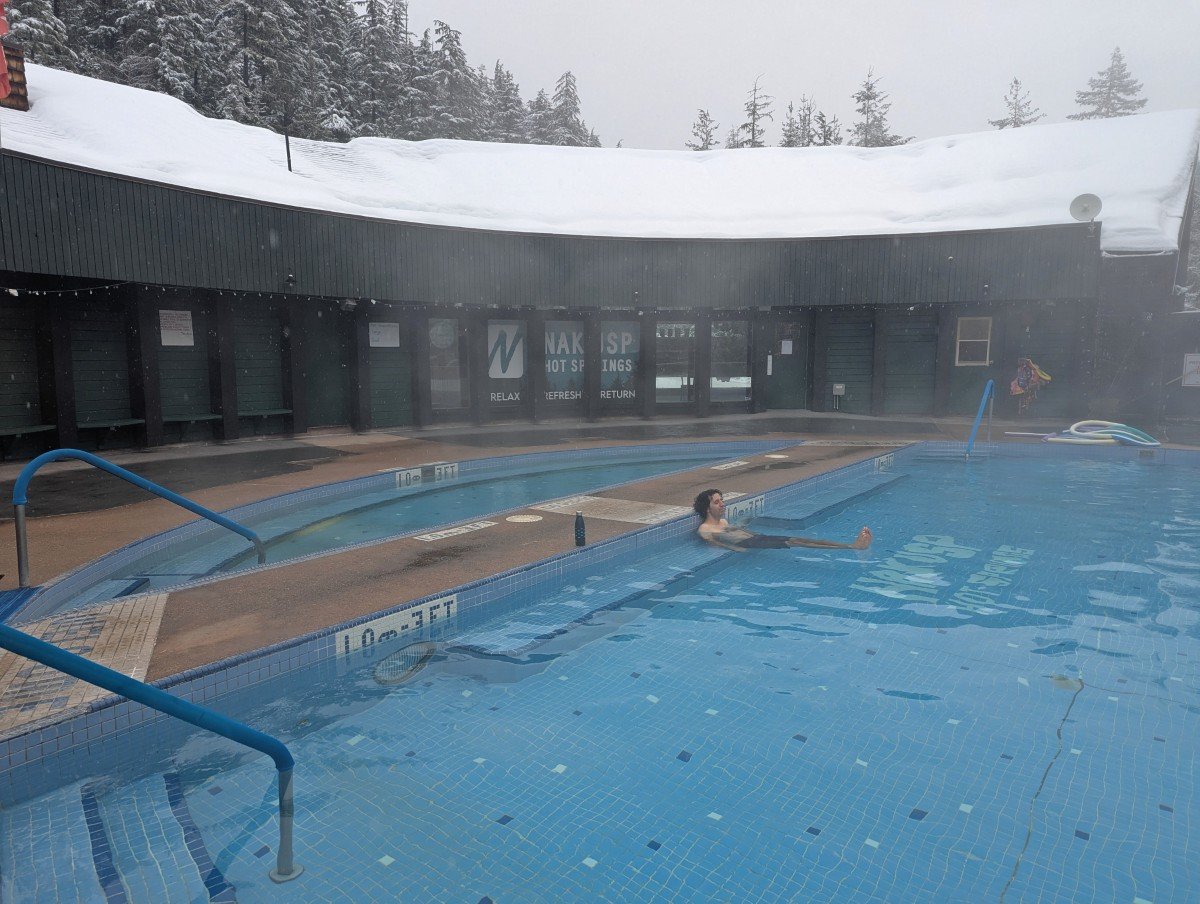 Nakusp Hot springs - two pools, one large, one small, in front of a curved single storey building with roof covered in snow