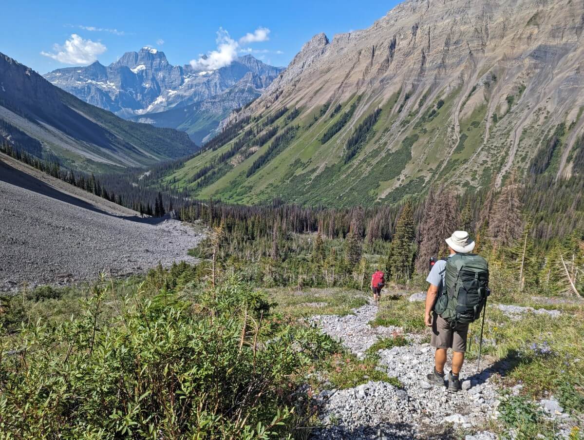 Back view of JR descending loose trail into river valley below large mountains